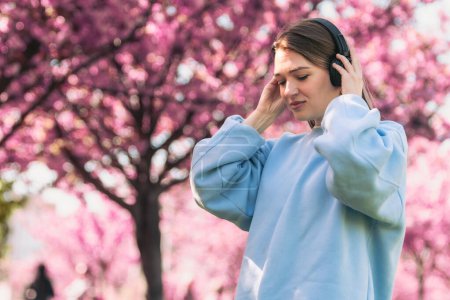 Téléchargez les photos : Élégant femme meloman écoute musique copie espace floraison sakura sur fond - en image libre de droit