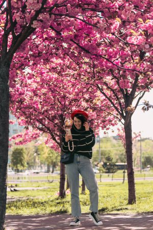 Téléchargez les photos : Jolie femme souriante posant devant les arbres sakura en fleurs copier l'espace - en image libre de droit