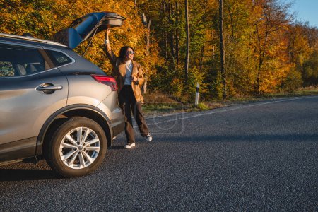 Téléchargez les photos : Femme souriante ferme le coffre de la voiture en automne saison. espace de copie - en image libre de droit