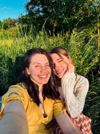 un selfie de deux jeunes femmes souriantes à l'extérieur en été