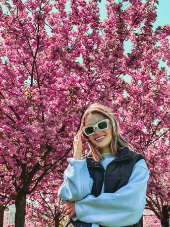 Téléchargez les photos : Portrait de belle femme souriante dans des lunettes de soleil fleur sakura sur fond - en image libre de droit
