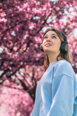 Téléchargez les photos : Élégant femme meloman écoute musique copie espace floraison sakura sur fond - en image libre de droit