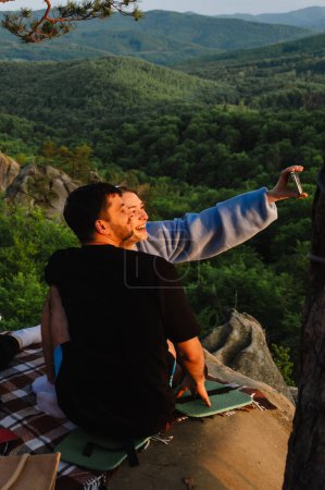 Téléchargez les photos : Couple heureux ayant rendez-vous à la falaise sur le coucher du soleil prendre selfie - en image libre de droit