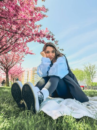 Téléchargez les photos : Jolie femme souriante posant devant les arbres sakura en fleurs copier l'espace - en image libre de droit