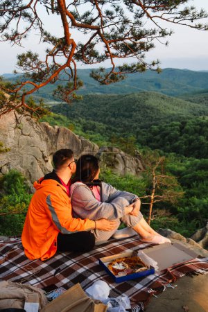 Téléchargez les photos : Couple heureux ayant rendez-vous à la falaise sur le coucher du soleil profiter du temps ensemble - en image libre de droit