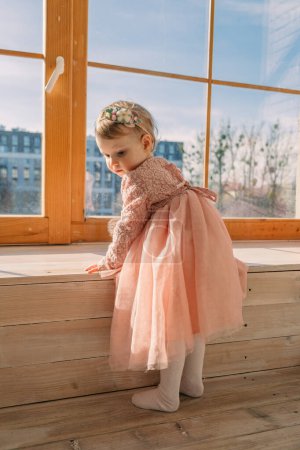 Téléchargez les photos : Petite fille mignonne en robe près de la fenêtre avec jouet ours - en image libre de droit
