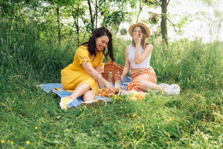 A couple of women chatting while sitting on blue picnic blanket in open air