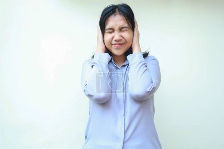 Téléchargez les photos : Déprimé asiatique jeune femme d'affaires couvrant les oreilles et la tête avec les yeux fermés, surmenage femme stressée portant chemise violette formelle debout isolé sur fond blanc - en image libre de droit