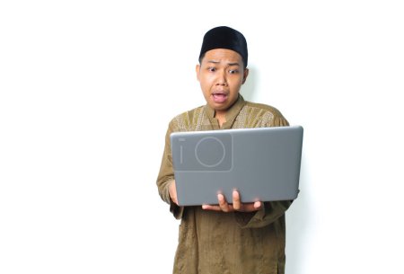 Photo for Shocked asian muslim man holding laptop looks scared isolated on white background - Royalty Free Image