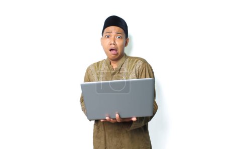 Photo for Shocked asian muslim man holding laptop looks scared isolated on white background - Royalty Free Image