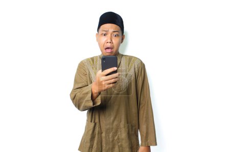 Photo for Shocked asian muslim man holding mobile phone isolated on white background - Royalty Free Image