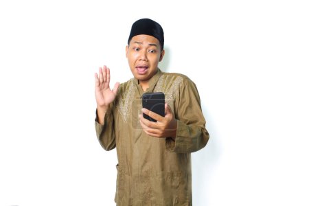 Photo for Asian muslim man holding mobile phone raising hand show shocked expression  isolated on white background - Royalty Free Image