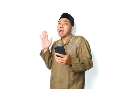 Photo for Asian muslim man holding mobile phone raising hand show shocked expression  isolated on white background - Royalty Free Image
