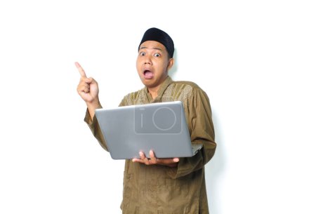 Photo for Shocked asian muslim man pointing to above with holding laptop isolated on white background - Royalty Free Image