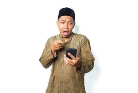 Photo for Shocked asian muslim man pointing finger at mobile phone isolated on white background - Royalty Free Image