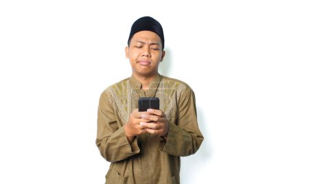 Photo for Anxious asian muslim man holding mobile phone show worry expression isolated on white background - Royalty Free Image