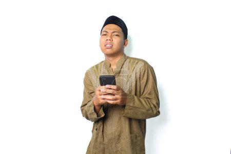 Photo for Anxious asian muslim man holding mobile phone show worry expression isolated on white background - Royalty Free Image
