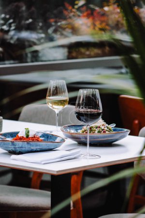 Foto de Una mesa para una cena con una copa y un vino tinto en el fondo de hierba verde - Imagen libre de derechos