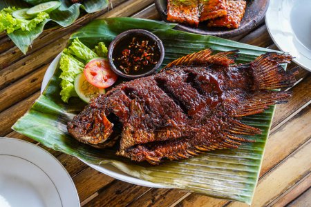 Photo for Grilled gurami or grilled gurame with red barbecue sauce, vegetables and chili sauce served on banana leaves - Royalty Free Image