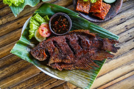 Photo for Grilled gurami or grilled gurame with red barbecue sauce, vegetables and chili sauce served on banana leaves - Royalty Free Image