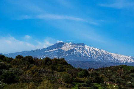Téléchargez les photos : Plan grand angle de l'Etna enneigée alors qu'elle éclate de bouffées blanches de vapeur contre un ciel intensément bleu - en image libre de droit