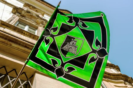Foto de Pegado a un poste una bandera verde y negra antigua con un logotipo del castillo en el centro revolotea durante un palio tradicional en Umbría - Imagen libre de derechos