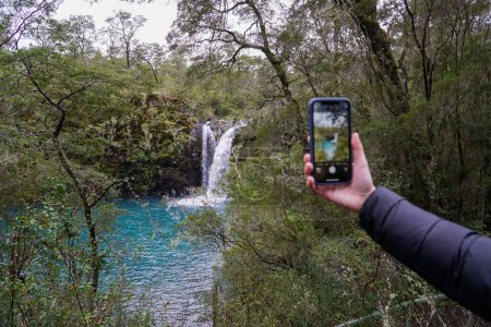 Téléchargez les photos : Une main floue prenant une photo de la belle cascade dans un lagon turquoise au sud du Chili. Photographie de voyage. - en image libre de droit
