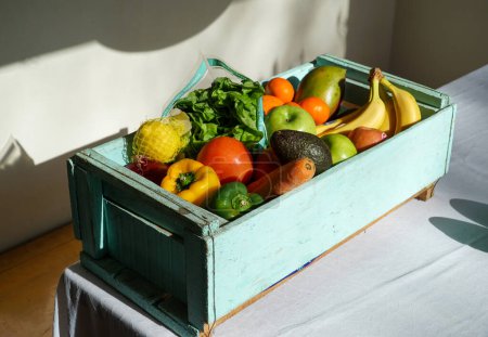 Téléchargez les photos : Récolte fraîche : Une caisse en bois peinte en bleu serein, débordant d'un assortiment de fruits et légumes vibrants. - en image libre de droit
