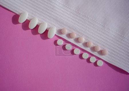 Photo for An arrangement of pills on a pink background, artfully presented with a white napkin. - Royalty Free Image