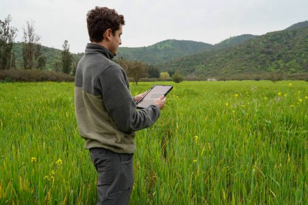 Téléchargez les photos : Agriculteur agricole surveillant les niveaux d'irrigation dans la plantation tout en se tenant dans le champ avec sa tablette. - en image libre de droit