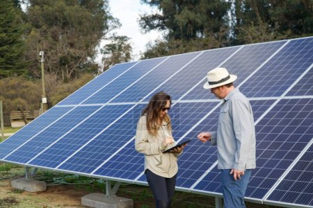 A farmer and a woman examining the solar panels in the field with a digital tablet.