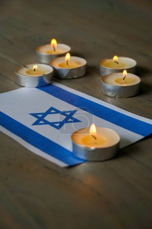 Téléchargez les photos : Un drapeau israélien illuminé par des bougies sur fond de bois sombre. - en image libre de droit