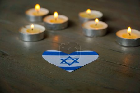 Candles burning atop an Israeli flag shaped as a heart.