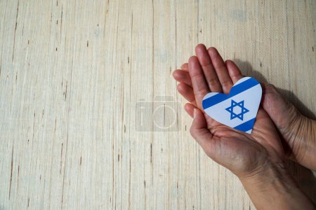 Téléchargez les photos : Des mains tendres bercent un drapeau israélien en forme de cœur, exprimant un profond sentiment d'amour et de connexion avec la nation. - en image libre de droit