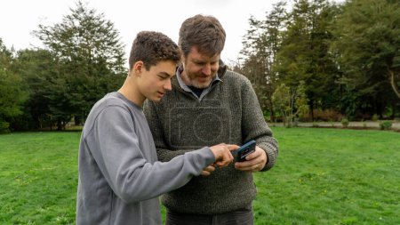 Foto de Vista de un adolescente mostrando algo en su teléfono a su padre, participando en un momento de intercambio digital y conexión. - Imagen libre de derechos