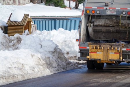 Téléchargez les photos : Rue enneigée avec un camion de collecte des déchets naviguant diligemment dans les conditions hivernales, assurant une bonne élimination des déchets. - en image libre de droit