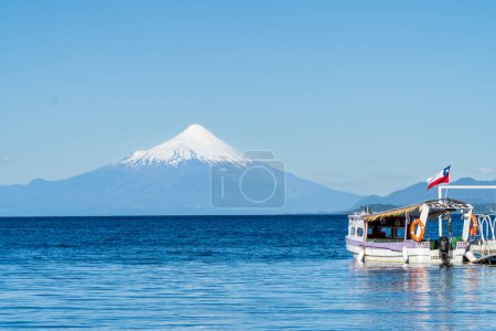 Téléchargez les photos : Vue panoramique sur la baie de Puerto Varas avec un lac calme et un volcan Osorno enneigé en arrière-plan. Tourisme bateau écrit "excursions en bateau". - en image libre de droit