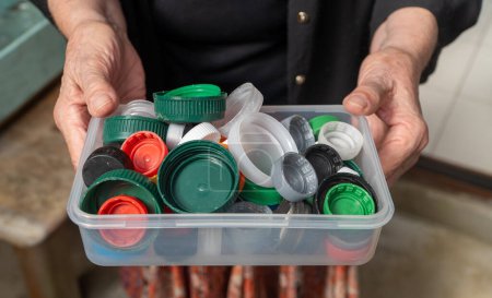 Elderly woman holding a container filled with plastic bottle caps.