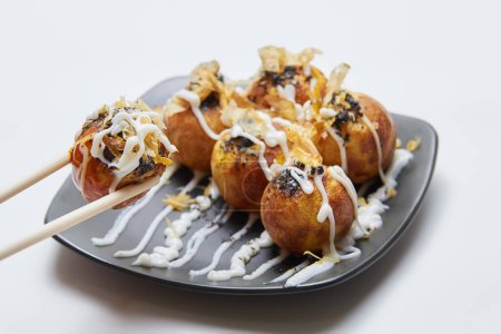 Photo for Takoyaki (octopus balls) on a plate isolated, one of the balls is picked up by chopsticks, isolated white background - Royalty Free Image
