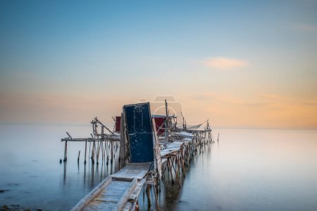 Téléchargez les photos : Piles en bois intégrées dans la mer et aider à la pêche, et les couleurs du coucher du soleil et la lumière - en image libre de droit