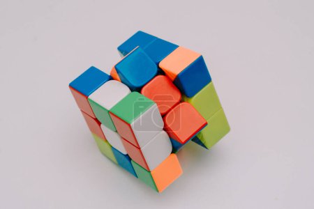 An unsolved 3x3 Rubik's cube stands on a white base