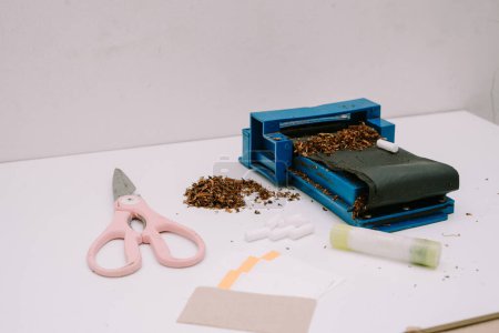 un outil à rouler les cigarettes composé d'un tuyau, de ciseaux, de papier et de colle à papier