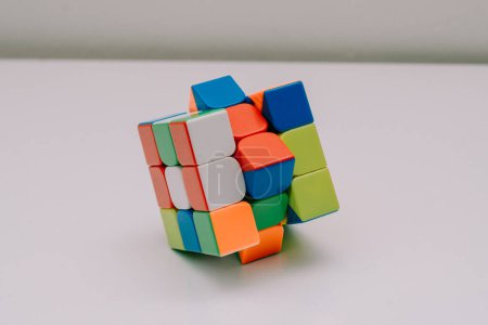 An unsolved 3x3 Rubik's cube stands on a white base