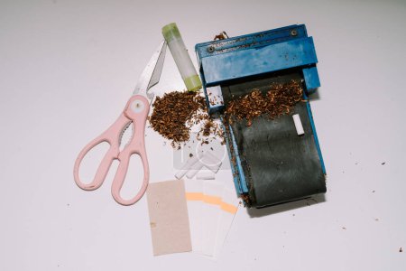 un outil à rouler les cigarettes composé d'un tuyau, de ciseaux, de papier et de colle à papier