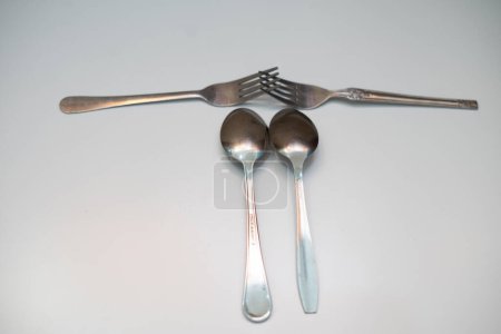 Dos cucharas y dos tenedores colocados sobre una base blanca