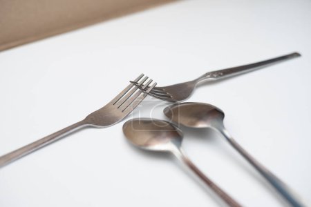 Dos cucharas y dos tenedores colocados sobre una base blanca
