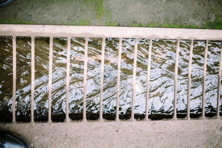 A stream of household runoff flows beneath, shielded by sturdy iron supports to prevent accidental slips, blending utility with safety