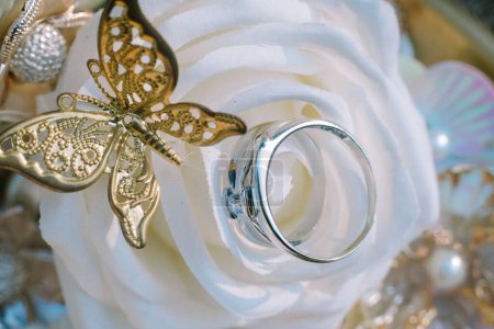 Ein Ehering mit einer zarten weißen Rose und einem Schmetterlingsmotiv aus Gold, das die ewige Liebe und die Schönheit der Vereinigung symbolisiert.