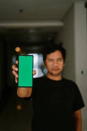Un homme tient un téléphone écran vert, le pointant vers la caméra