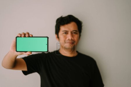 A man holds a greenscreen phone, pointing it towards the camera